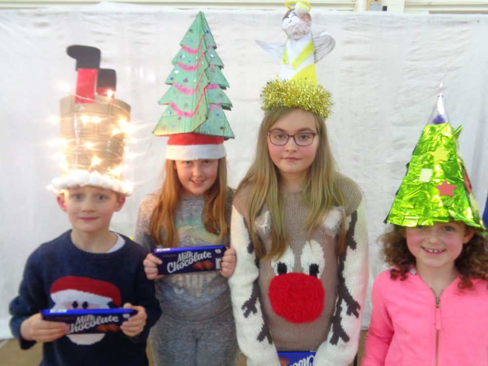Image of four children wearing homemade Christmas hats and each holding a large bar of chocolate.